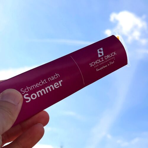 Hand hält Banderole mit Wassereis in den Himmel Werbung Druckerei bedruckt gebrandet mit Scholz-Druck Vorderseite zu sehen, Sonnenstrahl genaau am Eis